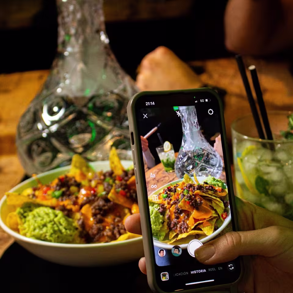 Un cuenco de nachos con guacamole y carne, un cóctel con lima y una mano capturando la escena con su móvil en modo historia.