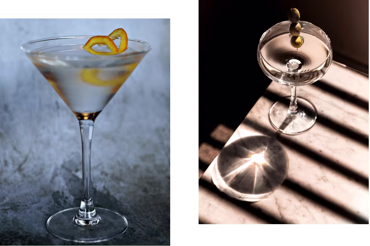 Two martini glasses: the left one with a lemon twist garnish on a textured surface, the right one with three olives skewered, casting a shadow on a striped marble table.