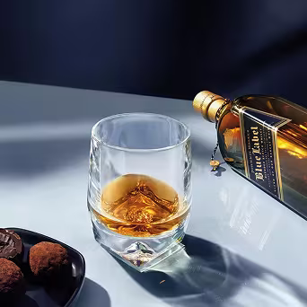 Botella de Johnnie Walker Blue Label junto a un vaso de whisky con una copa vacía