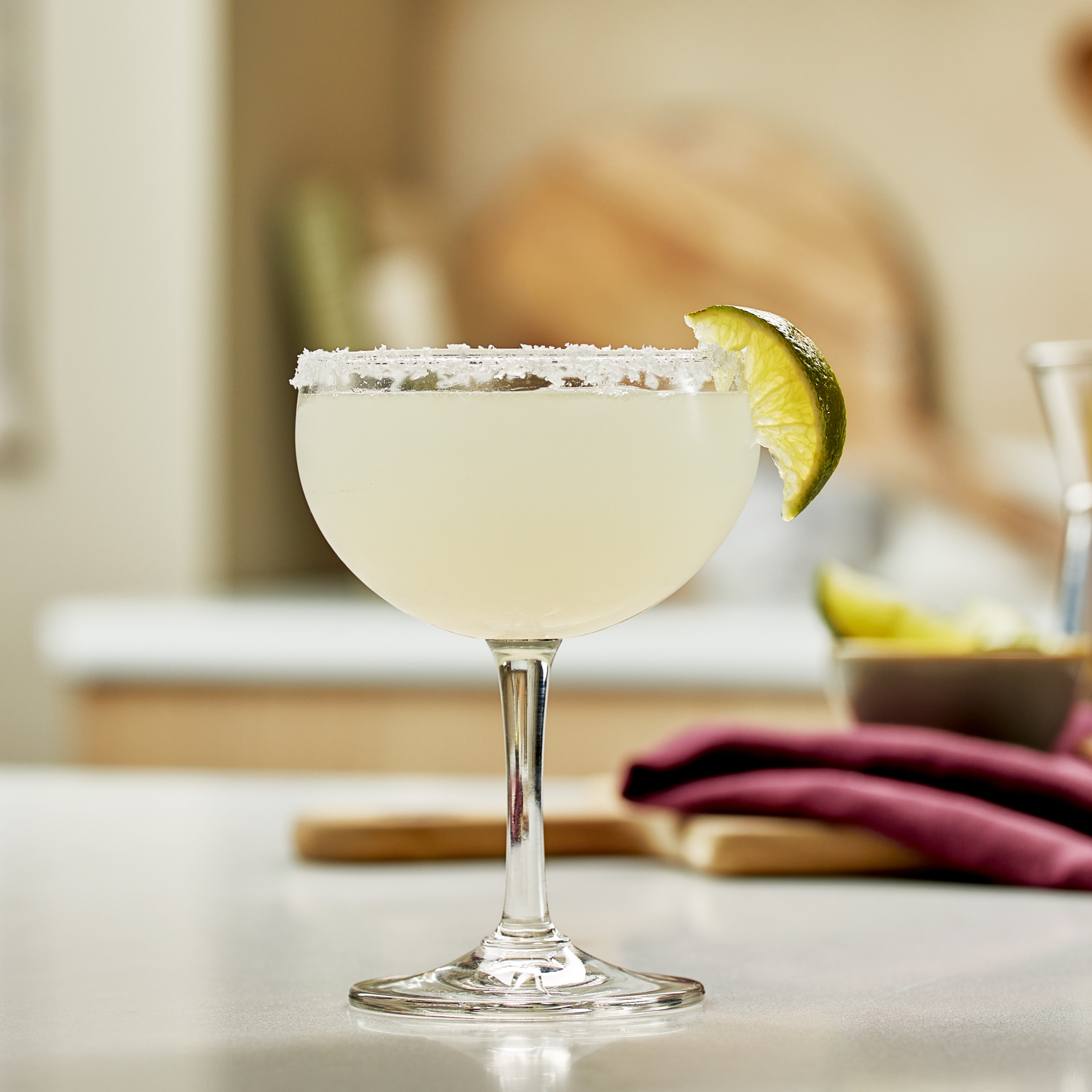 A margarita cocktail in a coupe glass with a salted rim and lime wedge garnish.