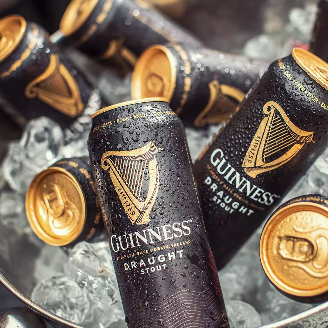 Several unopened and opened cans of Guinness Draught Stout rest on ice in a metal container, with condensation visible on the cans.