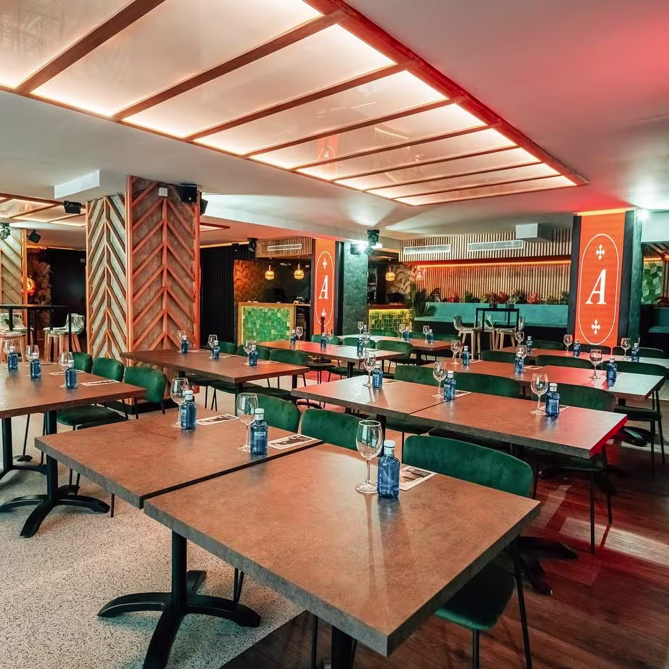 Espacio elegante y moderno en Antojo, con mesas preparadas y pantalla de fondo destacando el logo del lugar.