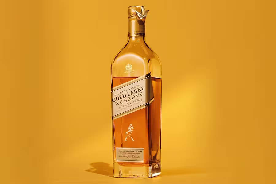 A bottle of Johnnie Walker Gold Label Reserve blended Scotch whisky stands upright against a solid yellow background.
