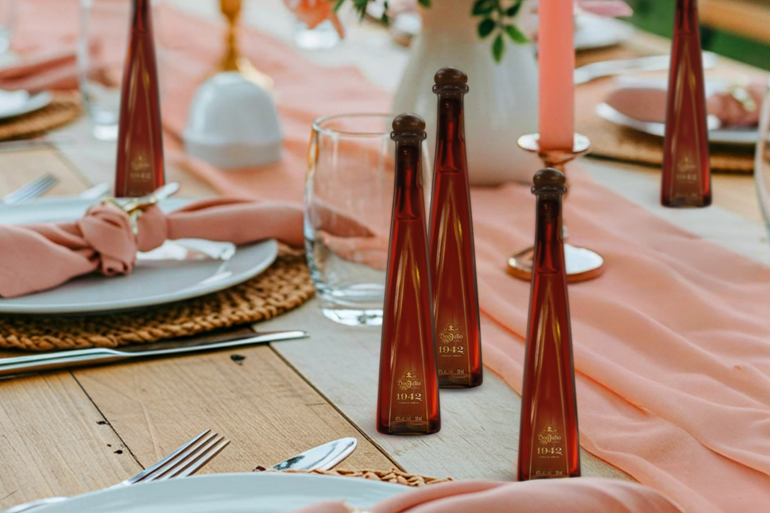 A table set for a meal with plates, glasses, cutlery, pink napkins, and several small brown bottles arranged upright on the table runner.