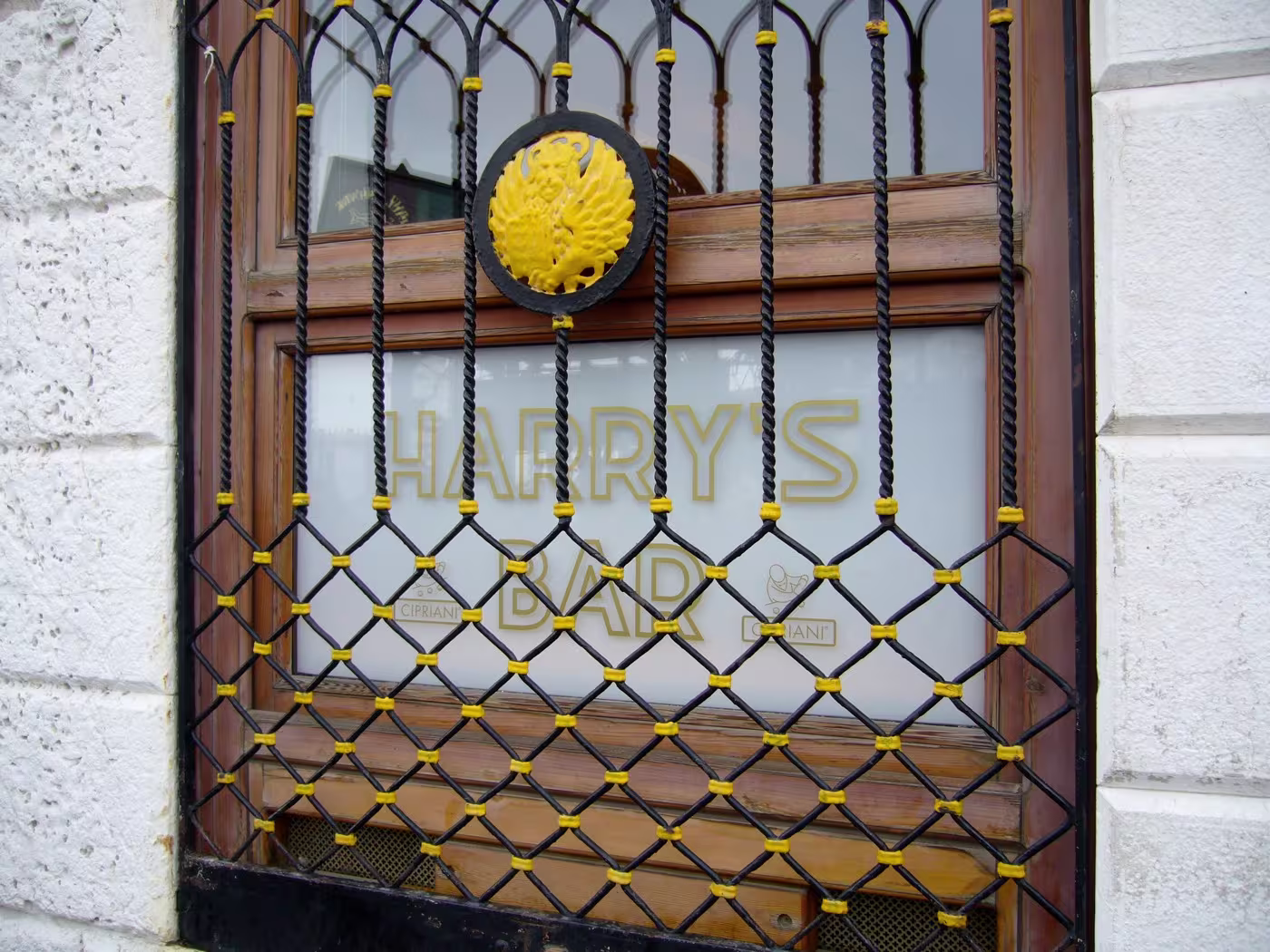 A window with frosted glass displaying the words Harrys Bar, partially obscured by a black and yellow decorative metal grate.