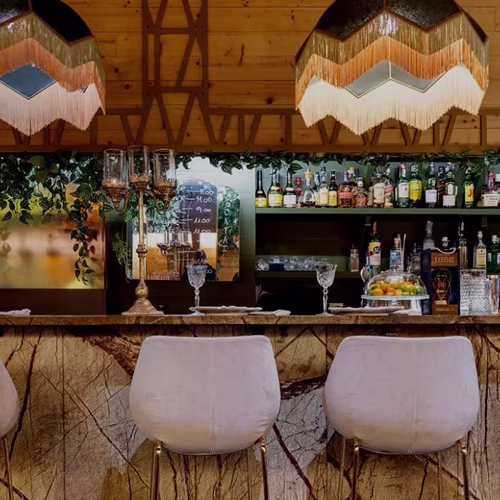 La barra de Vuelve Carolina combina madera, mármol y vegetación, creando un ambiente sofisticado con iluminación cálida y un toque de elegancia vintage.