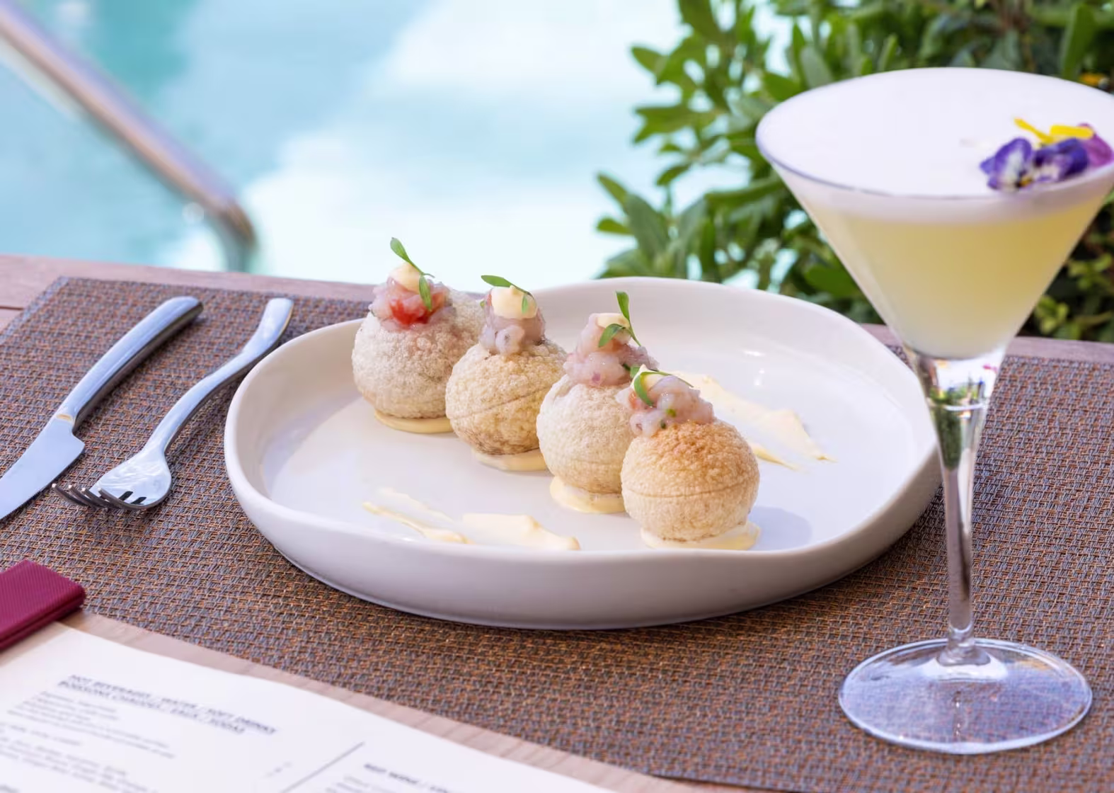 En La Dolce Vitae del Majestic Hotel, unas esferas crujientes rellenas de tartar de langostinos acompañan a un sofisticado cóctel junto a la piscina.