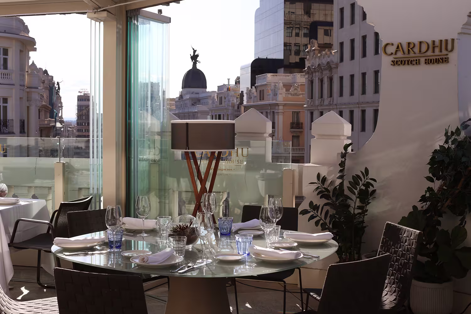 The Bar | Picalagartos - Mesa redonda preparada para una comida al aire libre, con vistas a la Gran Vía madrileña y un elegante montaje de copas y platos.