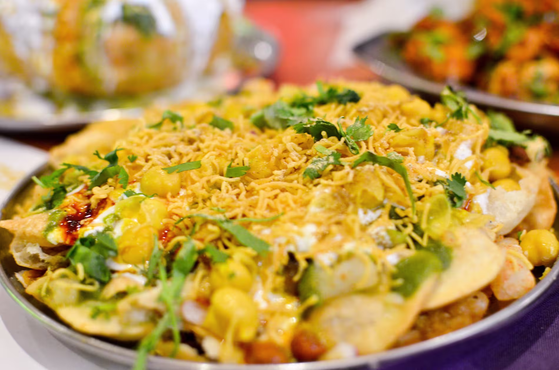 A plate of Indian chaat topped with sev, chopped coriander, corn, yogurt, and various chutneys.
