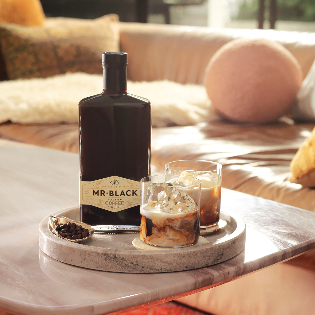 Mr Black Cold Brew Coffee Liqueur bottle with two iced coffee cocktails and a bowl of coffee beans on a marble tray