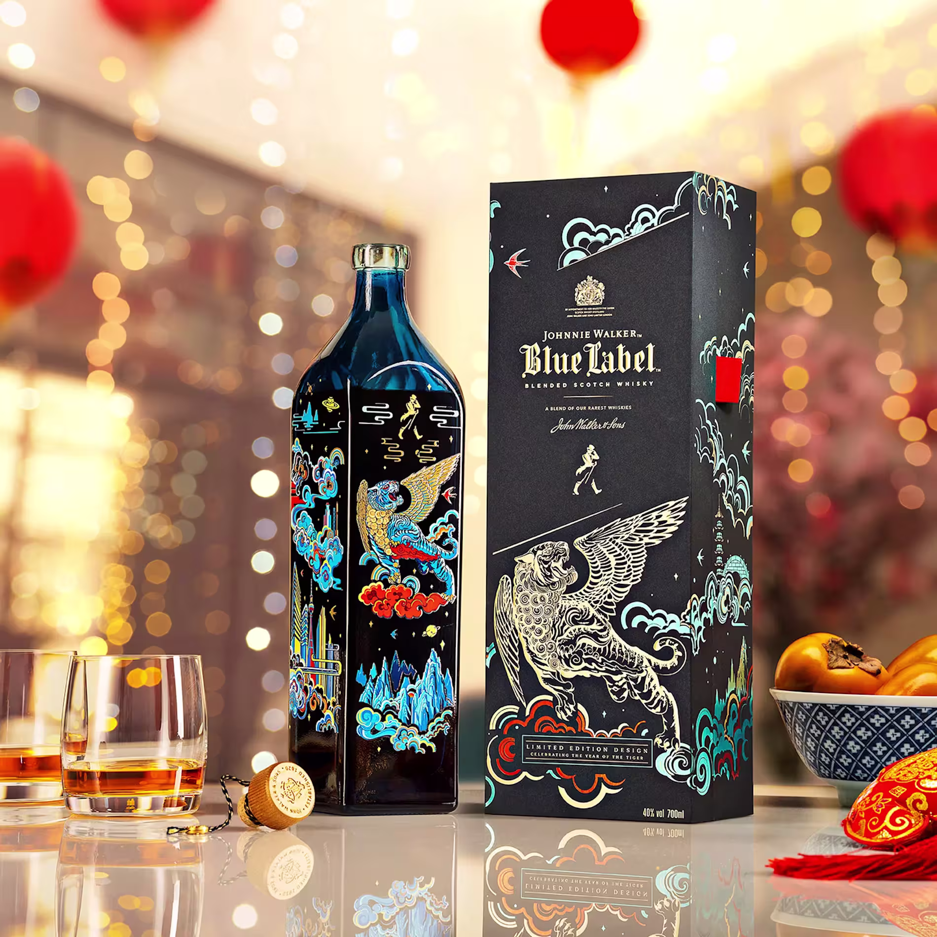 A Johnnie Walker Blue Label bottle and its decorative box sit on a table with two glasses of whisky, festive lights, and Chinese New Year decorations in the background.