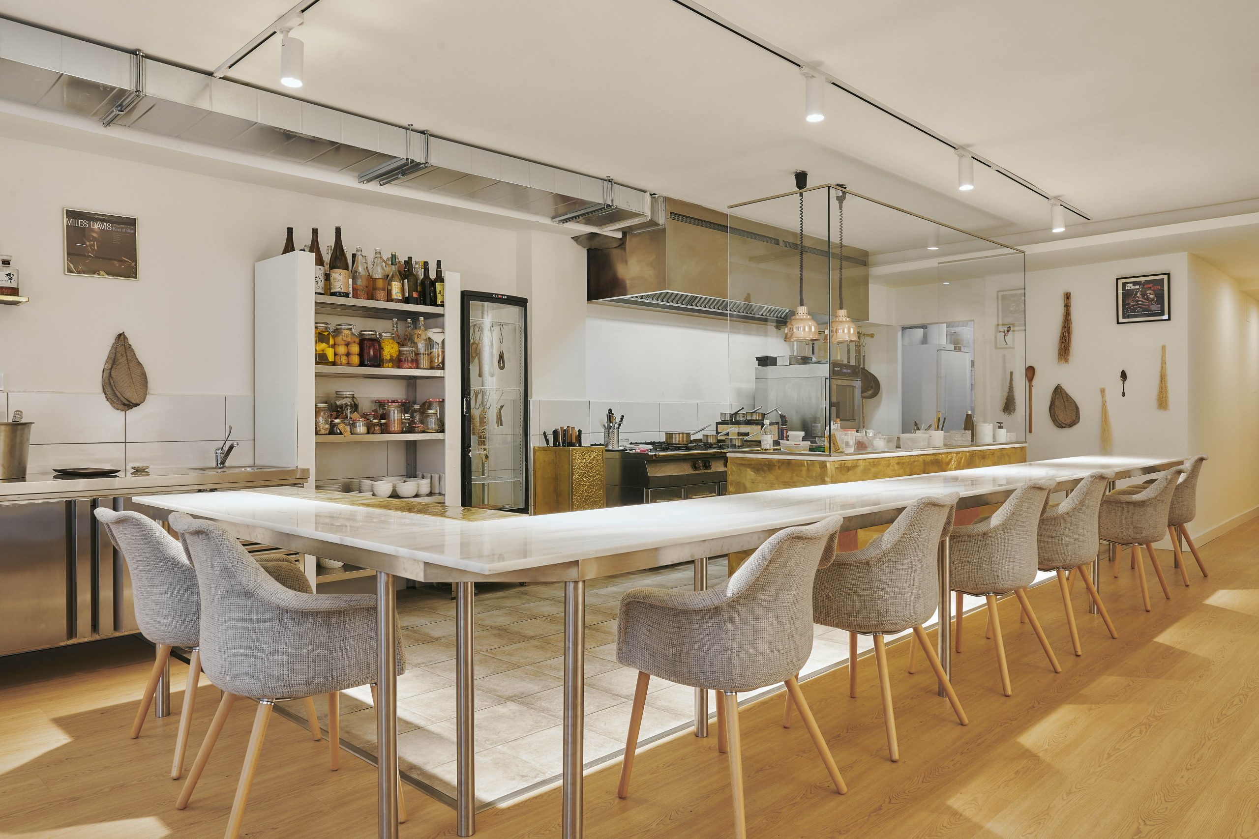 Un espacio gastronómico elegante con cocina abierta, mesa comunal de mármol y sillas tapizadas, combinando diseño moderno con toques artesanales.