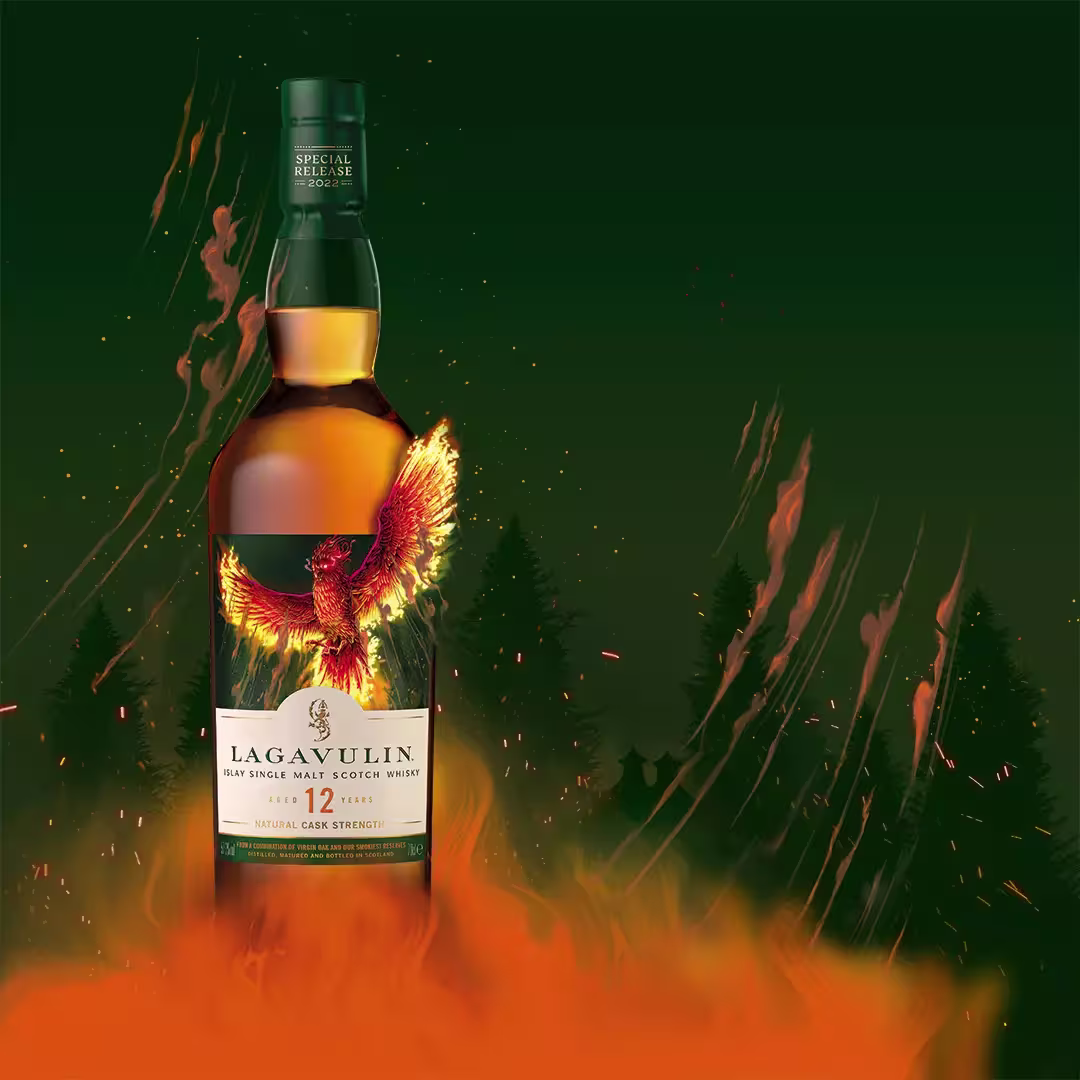 A bottle of Lagavulin 12 Year Old Scotch whisky stands amid orange flames and embers, with a fiery phoenix illustrated on the label and smoke rising in the background.