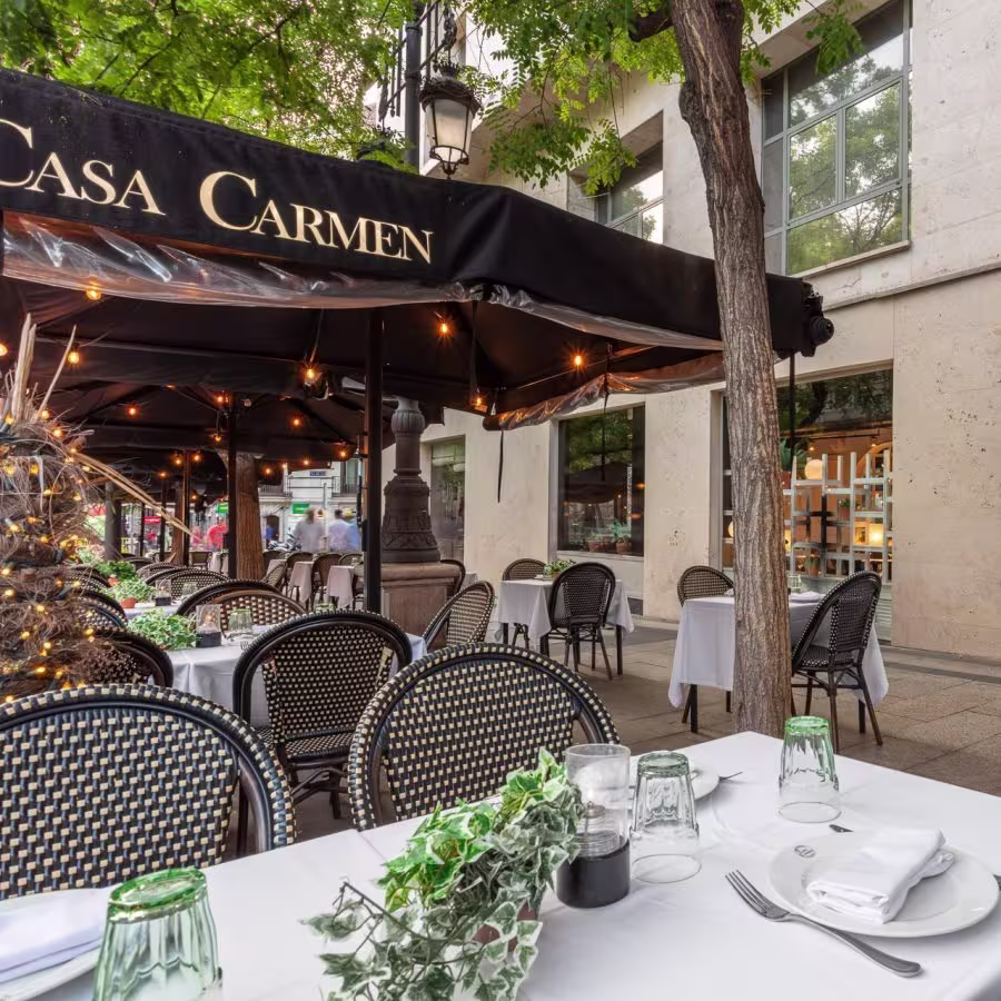 Terraza elegante de Casa Carmen en Madrid, con mesas decoradas y ambiente acogedor bajo sombrillas iluminadas.
