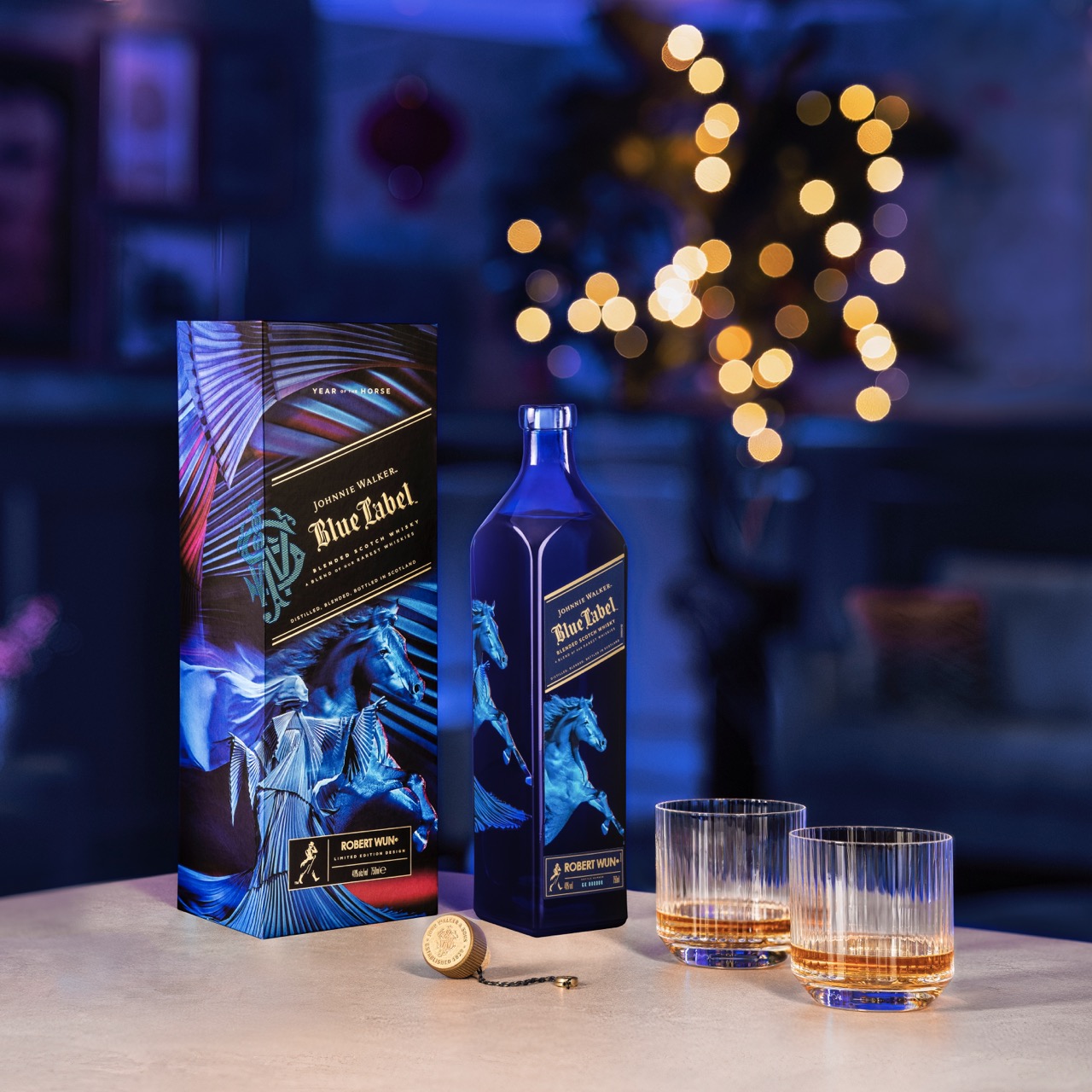 A bottle of Johnnie Walker Blue Label with its box and two filled whiskey glasses on a table, with warm, blurred lights in the background.