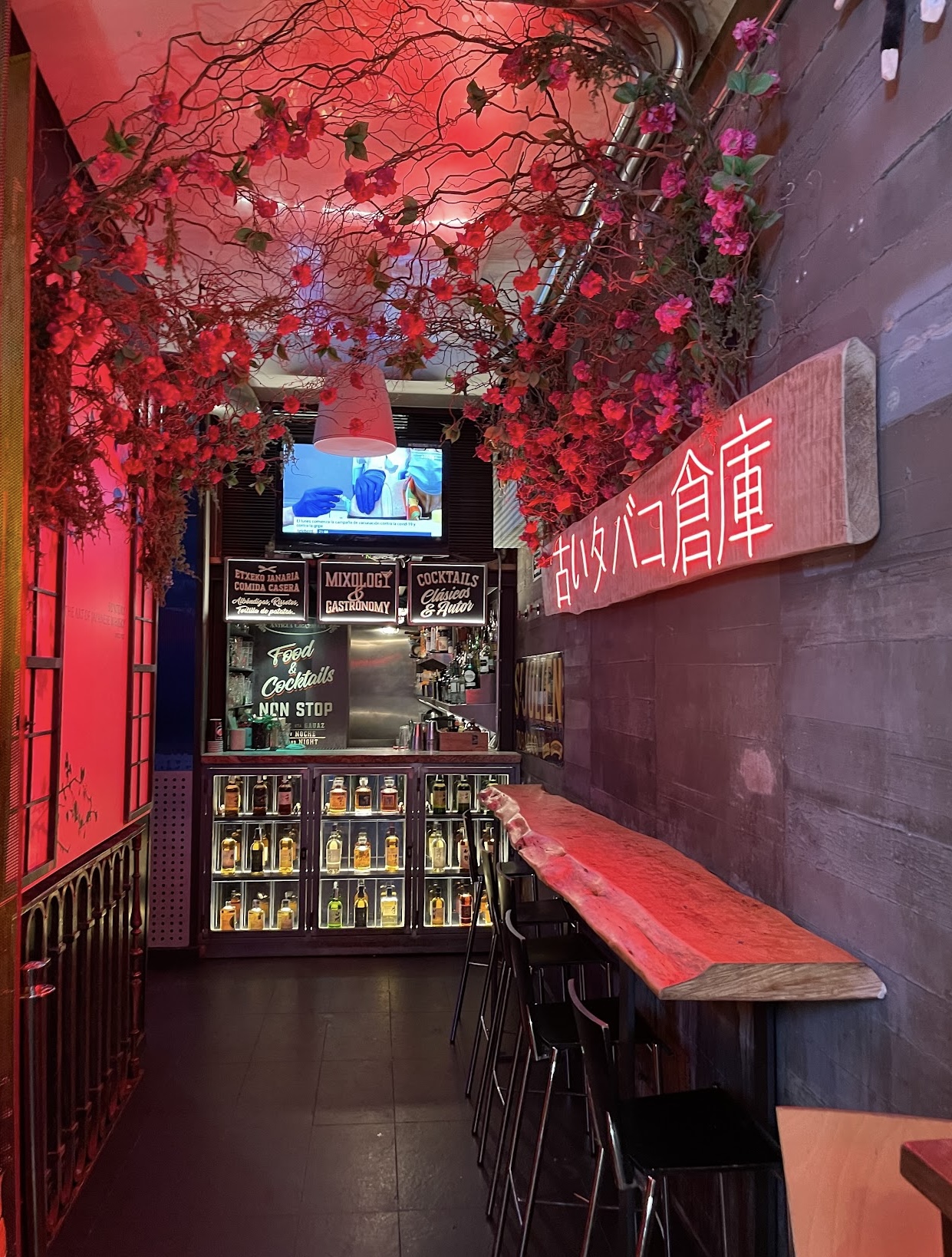 Barra de Antigua Cigarrería, decorada con neón rojo y un techo cubierto de flores, creando un ambiente único y moderno para disfrutar cócteles clásicos.