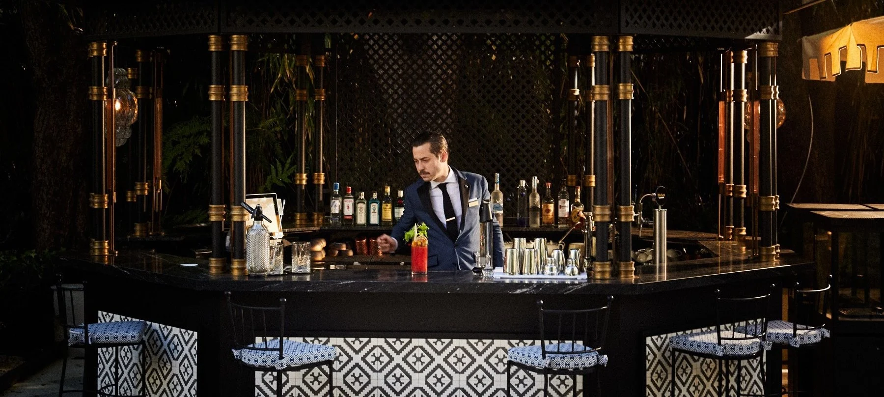 Bar exterior del Restaurante Santo Mauro, con decoración elegante en tonos oscuros y un bartender preparando un cóctel en un ambiente exclusivo.