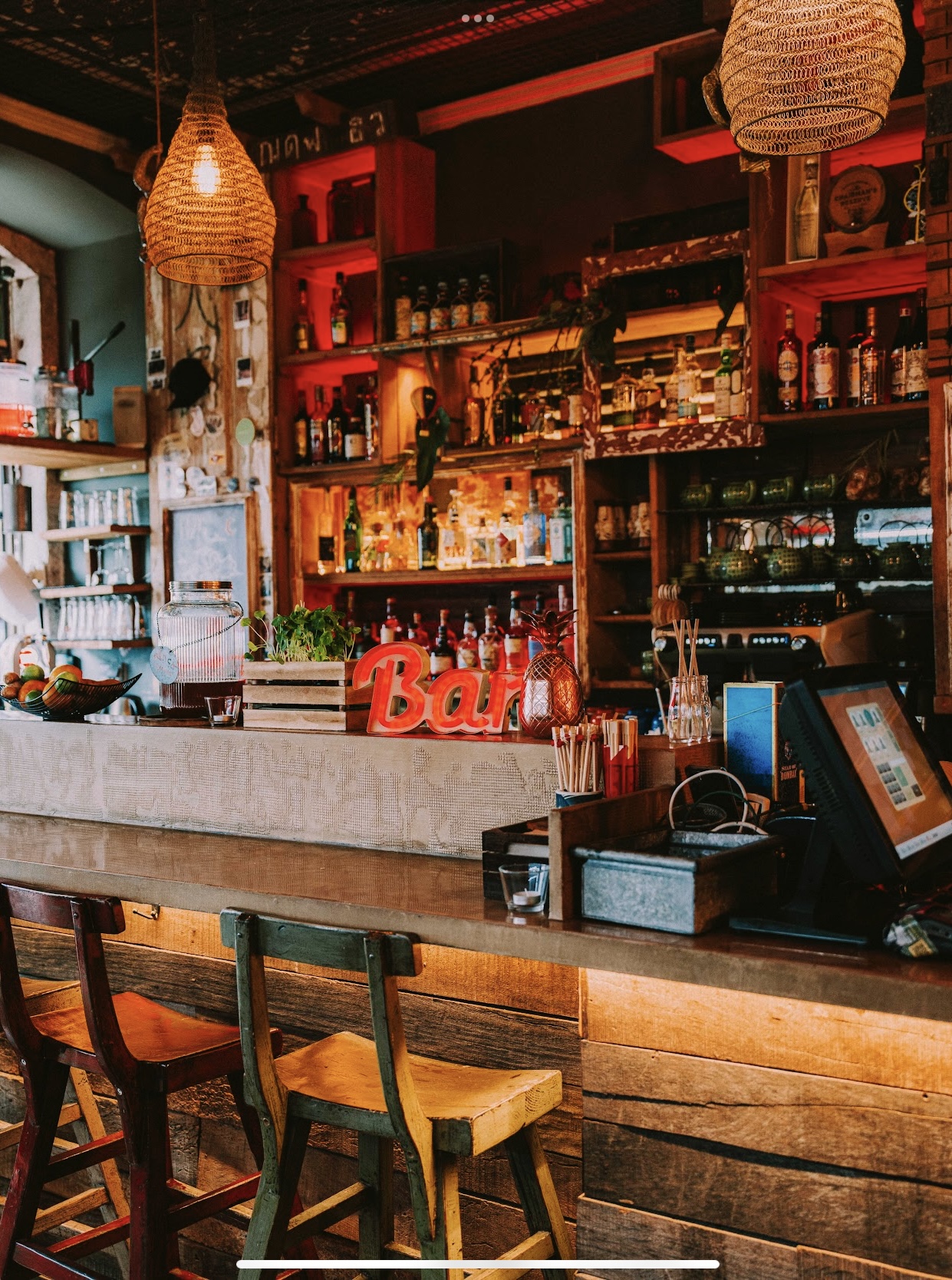 Interior de Boa Bao, con barra de madera rústica, taburetes de colores, iluminación cálida y estanterías llenas de botellas y detalles decorativos.