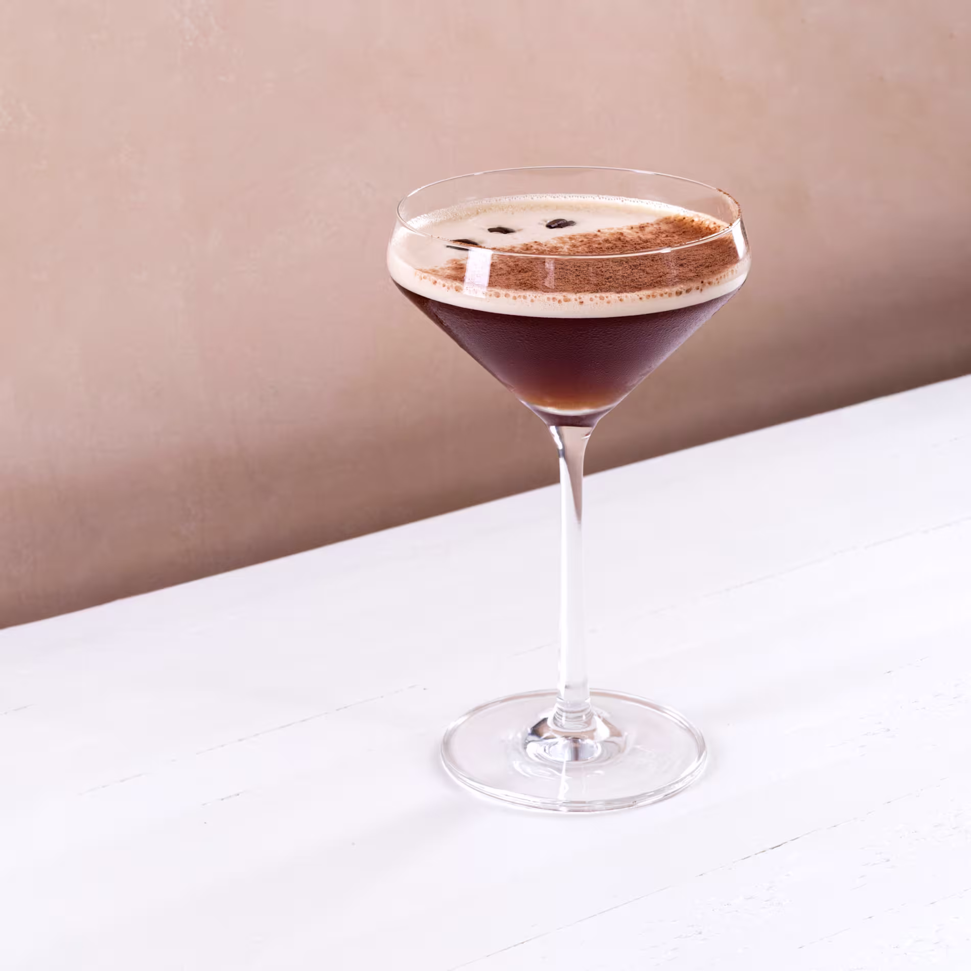 Espresso martini cocktail in a coupe glass garnished with coffee beans on a white table