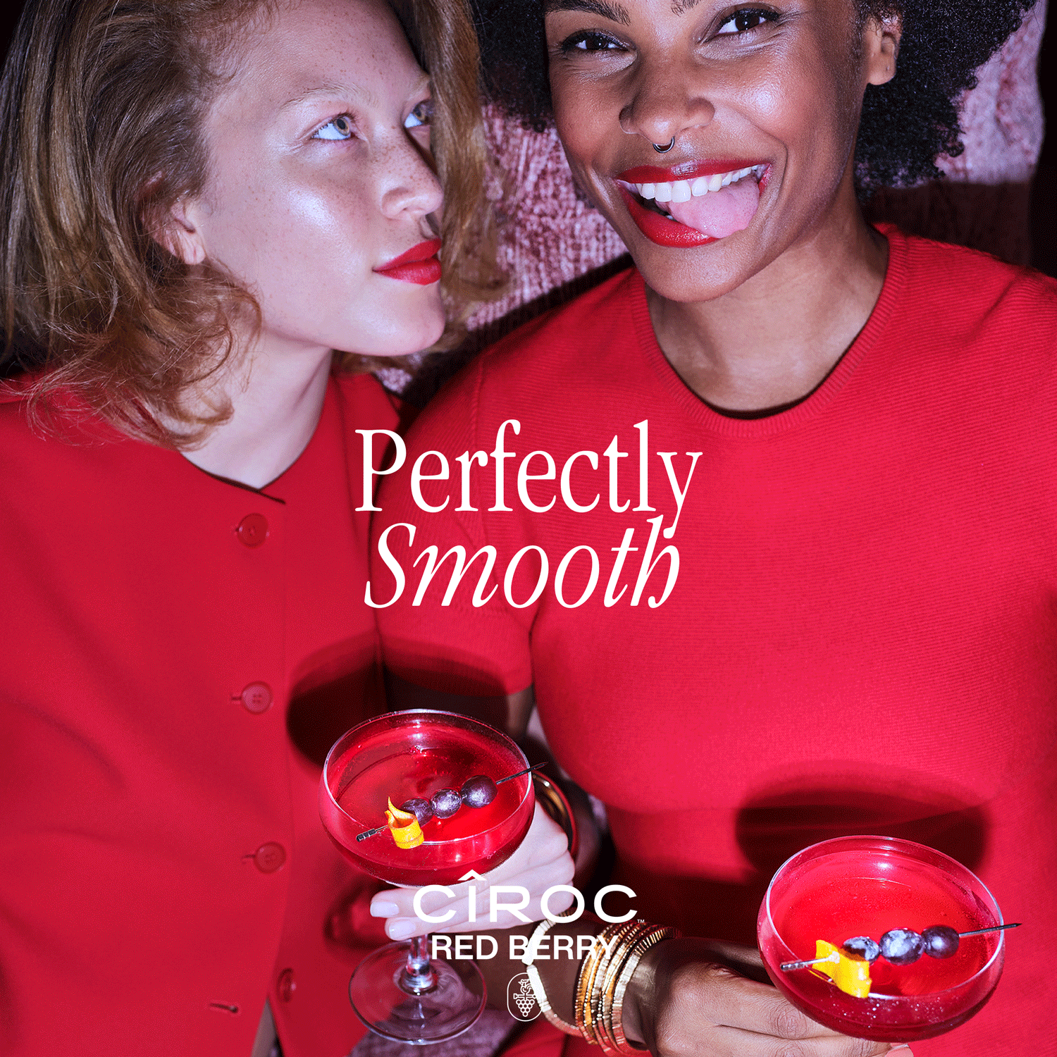 Two women in red outfits hold red cocktails with garnish, smiling and posing together. Text reads “Perfectly Smooth” and “Ciroc Red Berry.”.