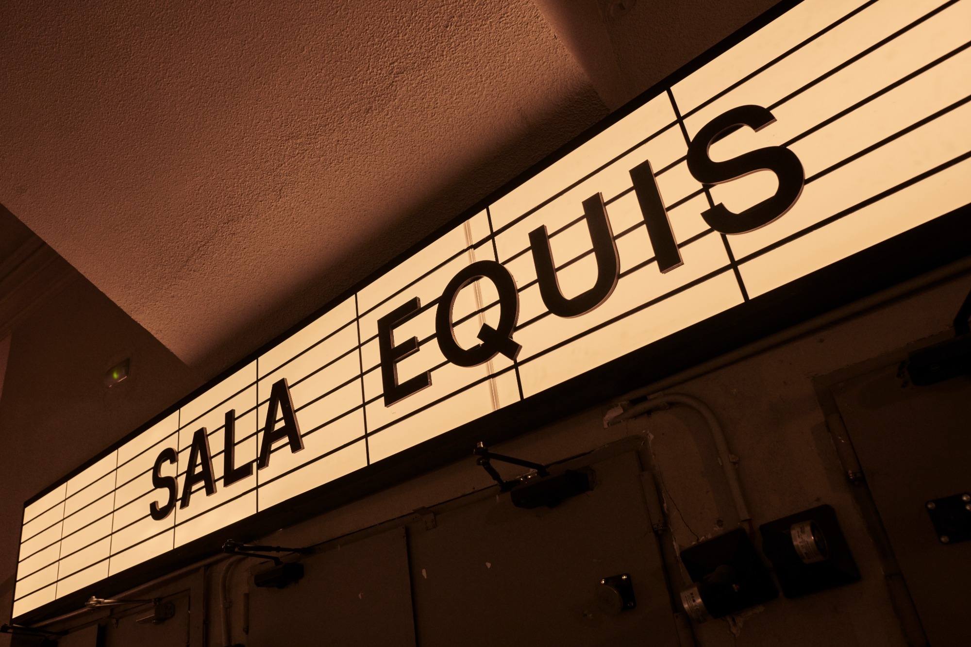 The Bar | Sala Equis - Primer plano del cartel iluminado de "Sala Equis" en letras grandes, destacando la entrada del local con una iluminación cálida y acogedora.