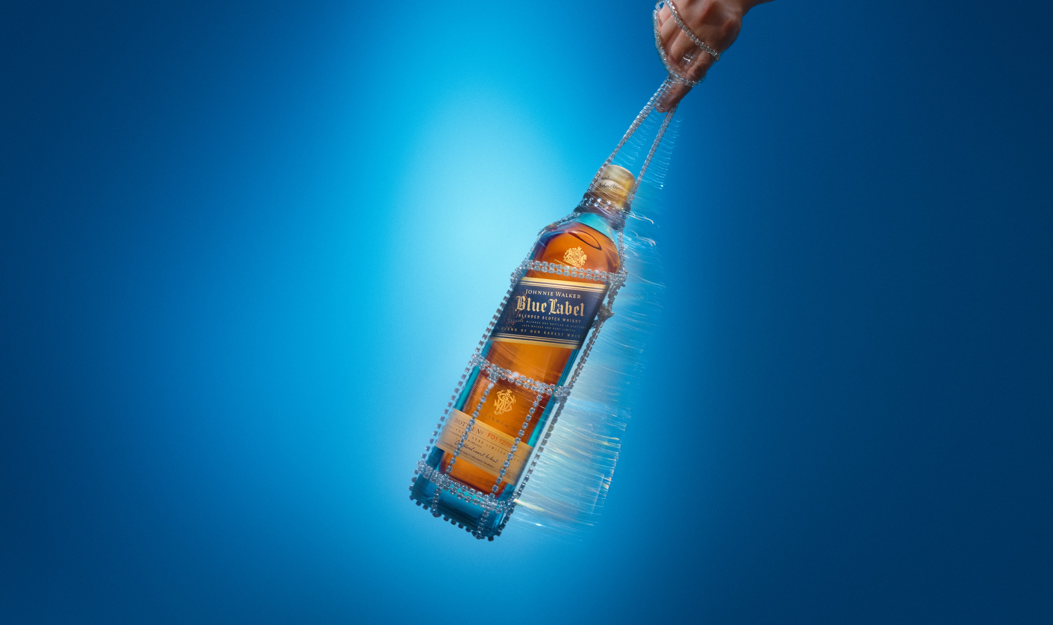 Una botella de Johnnie Walker Blue Label sobre un fondo azul, con una luz suave que resalta su distintiva etiqueta azul y dorada.