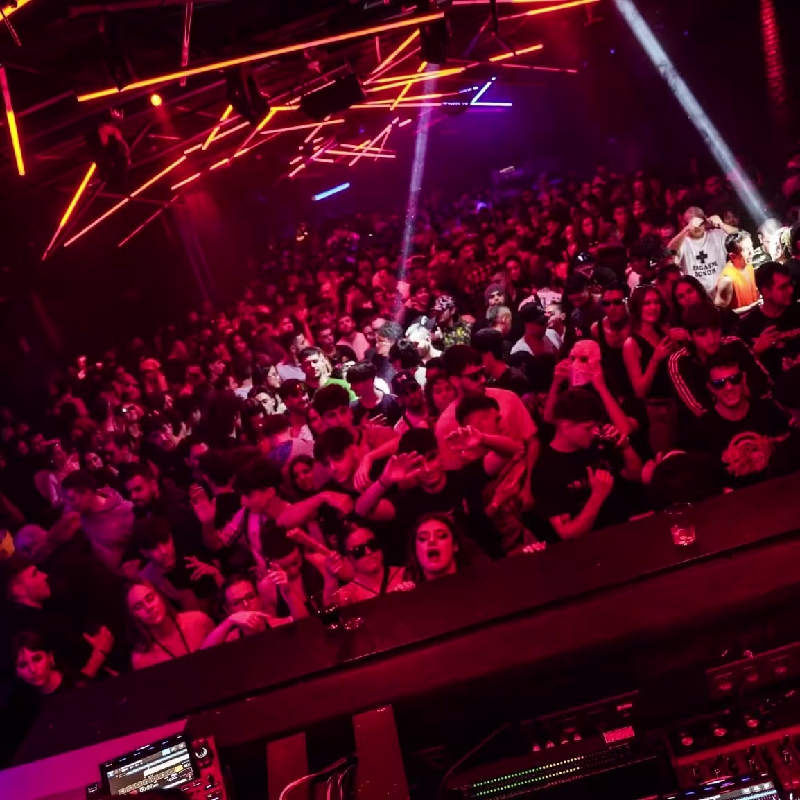 Fiesta a tope en Sala Sonora: luces rojas, DJ en cabina y una pista llena vibrando con la música electrónica.