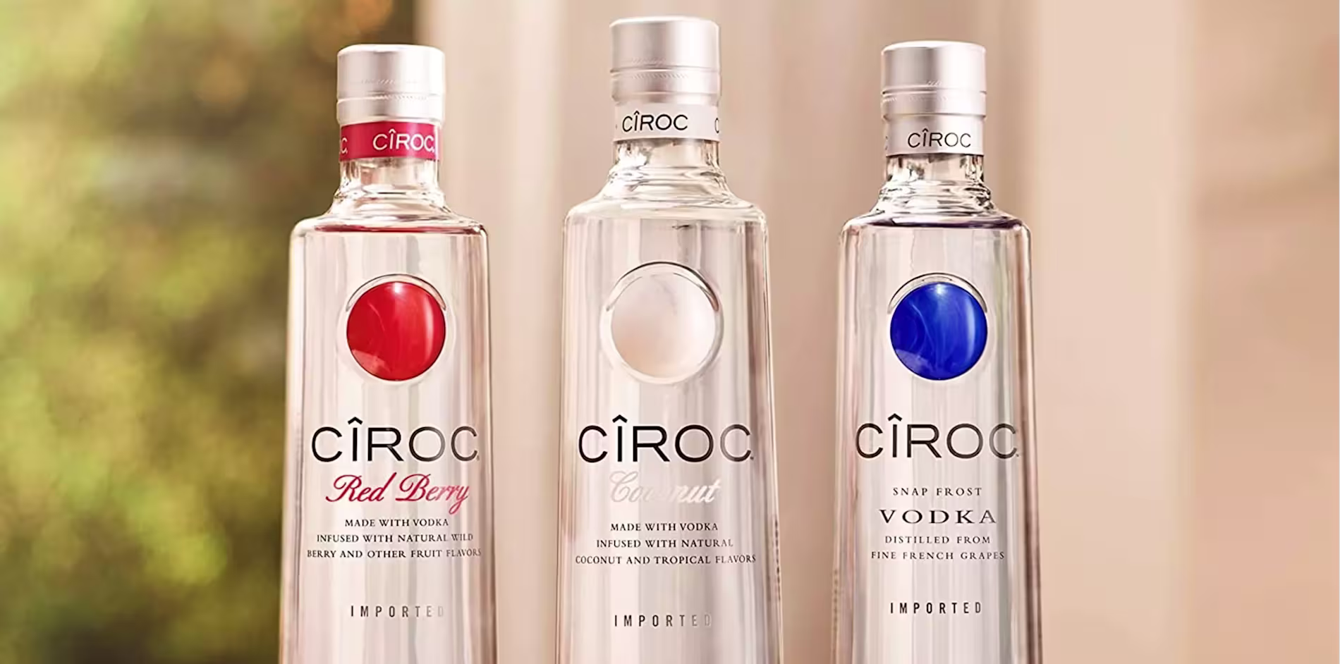 Three Ciroc vodka bottles—Red Berry, Coconut, and Snap Frost—stand side by side on a surface with a blurred background.