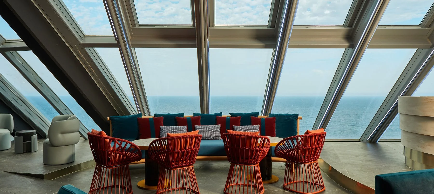 Sofás coloridos y sillas de diseño en Noxe, W Hotel, con un ventanal panorámico que enmarca impresionantes vistas al mar.