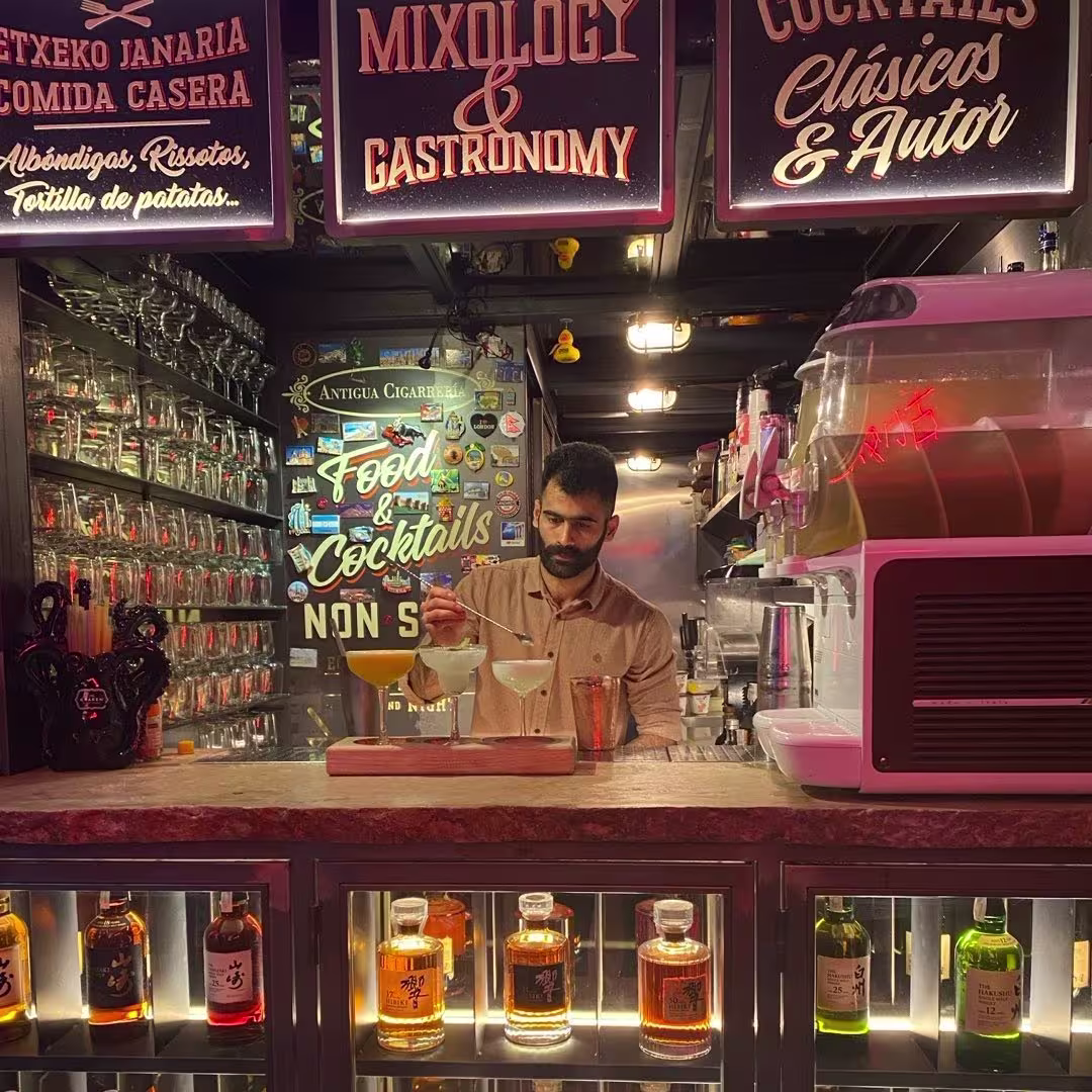 Barman preparando cócteles en Antigua Cigarrería, rodeado de botellas iluminadas y carteles de mixología y gastronomía.