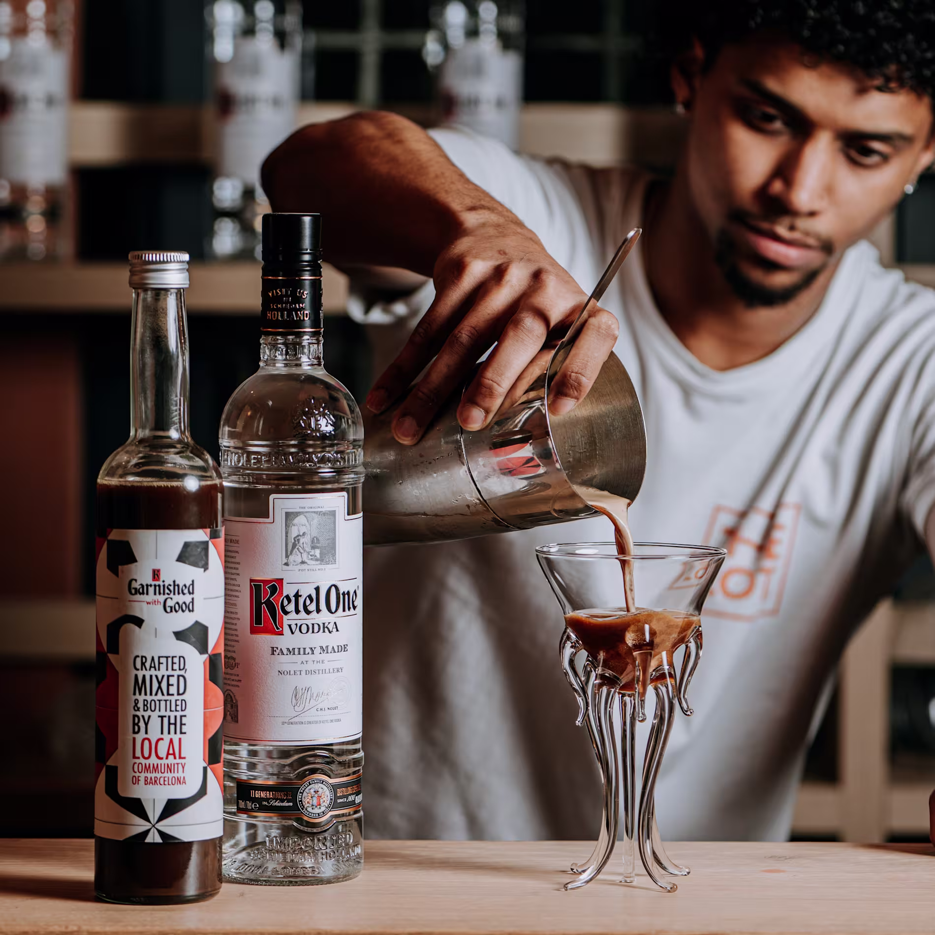 Bartender sirviendo un cóctel en copa artística con Ketel One y Garnished with Good. Creatividad líquida en estado puro.