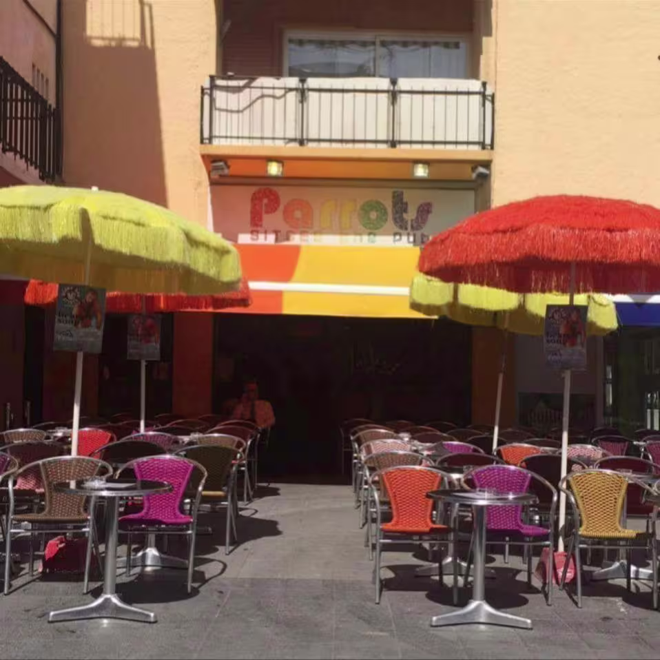 Terraza de Parrots Sitges, llena de color y sombrillas vibrantes, ideal para disfrutar de una bebida al aire libre.