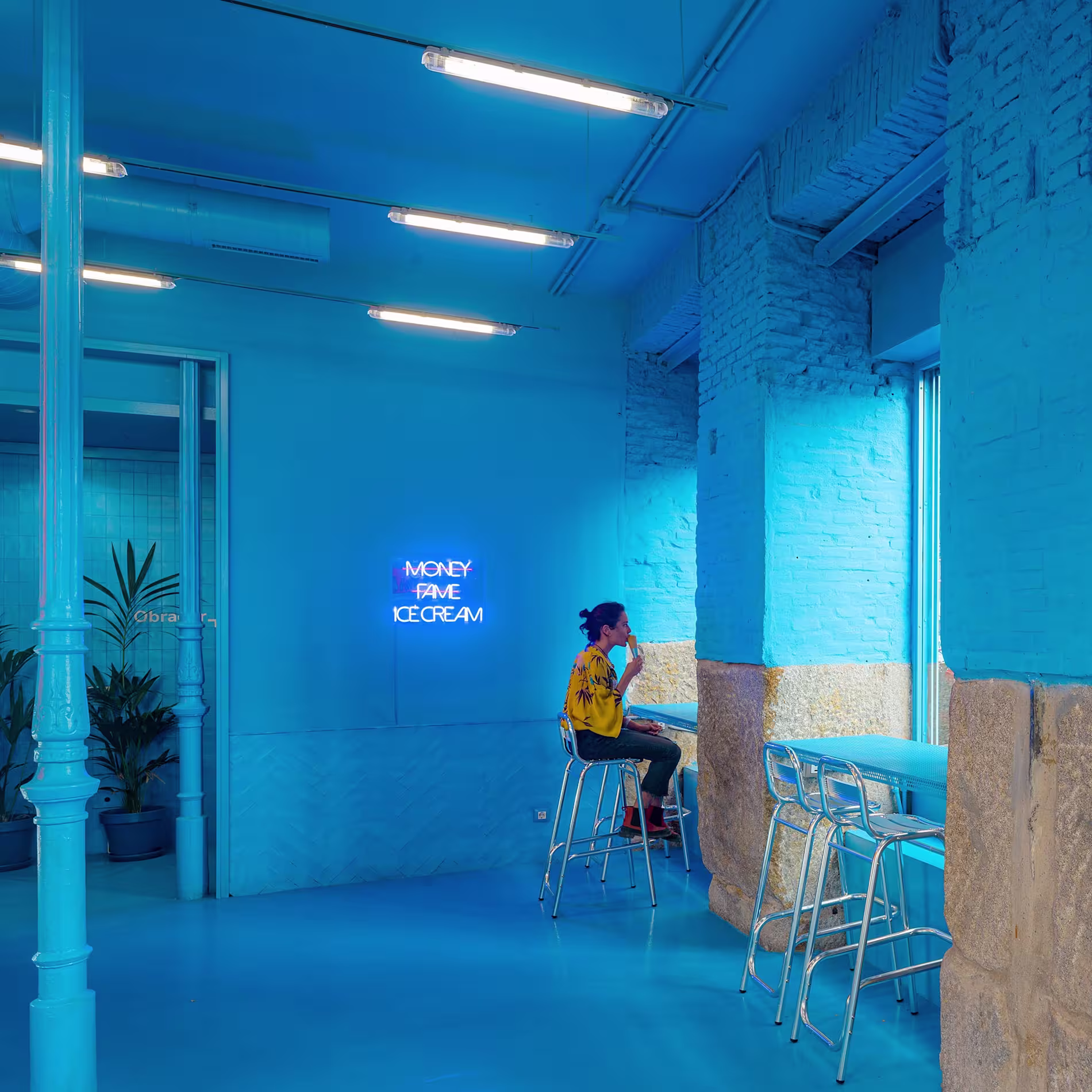 Interior azul eléctrico en Brando Helados, con neón en la pared y taburetes metálicos frente al ventanal. Un espacio vibrante para disfrutar sin prisas.