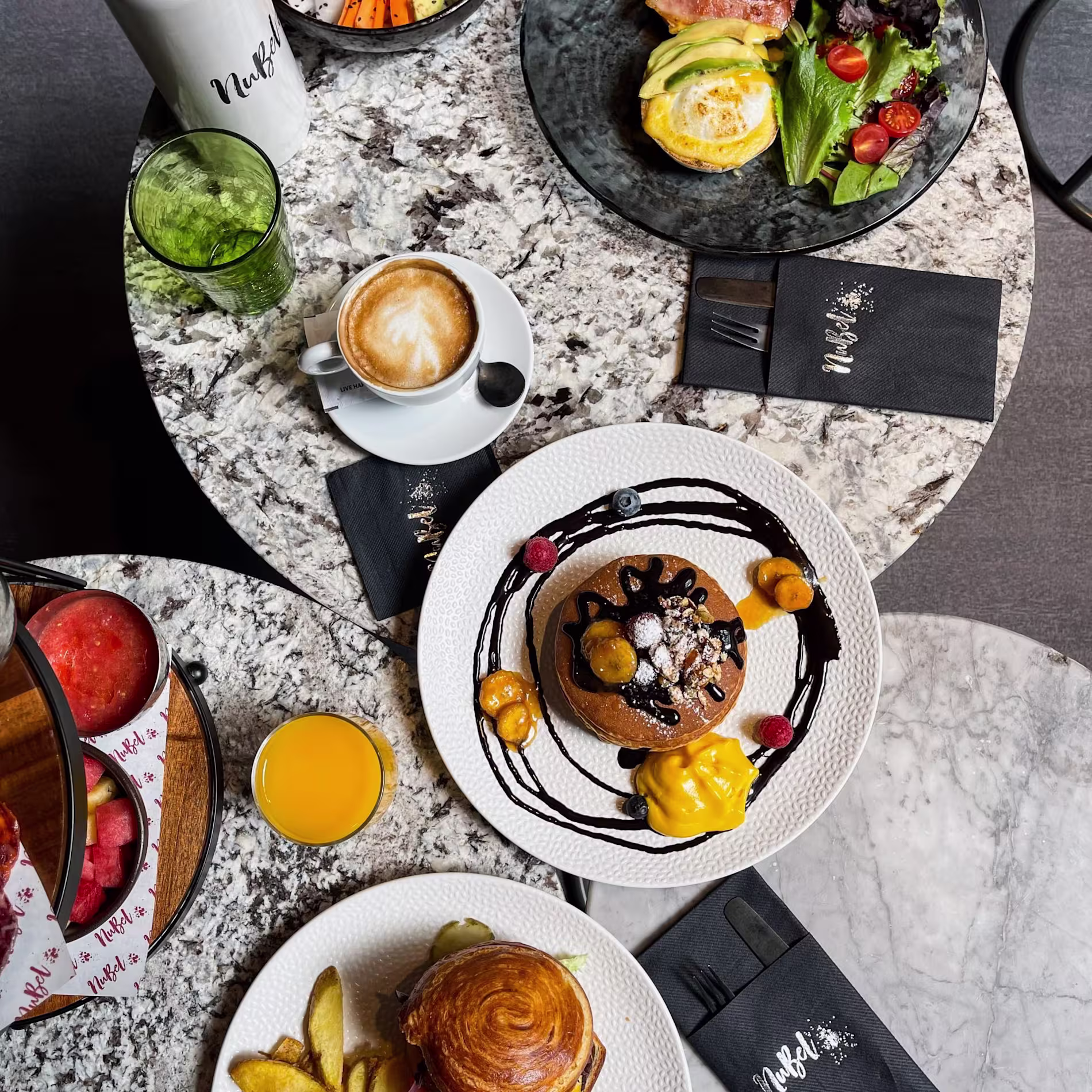 NuBel presenta una mesa vibrante con pancakes, burgers, bowls y zumos sobre mármol, ideal para un brunch colorido y lleno de sabor.