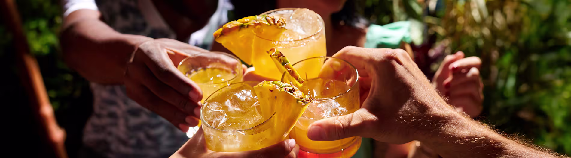Grup de mâini care toastează cu cocktailuri tropicale cu rom garnisite cu ananas în aer liber