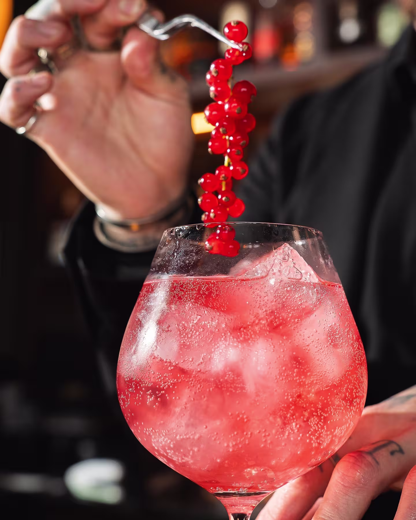 Cóctel burbujeante en Coya Barcelona, decorado con una rama de grosellas rojas, servido en una copa elegante con un toque artístico.