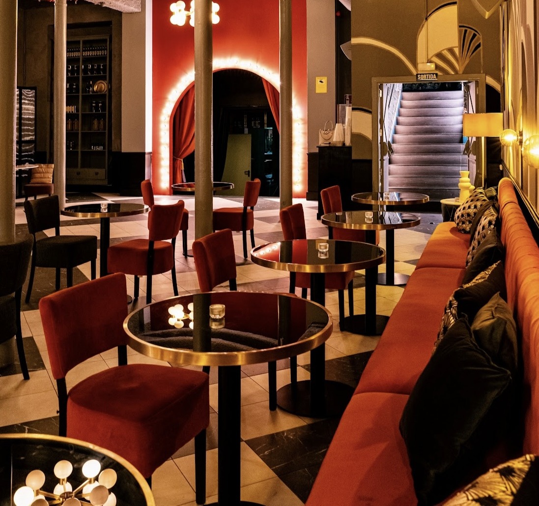 Interior de Club 61, con mesas negras y sillas rojas, iluminación cálida y un arco iluminado que enmarca una cortina roja al fondo.