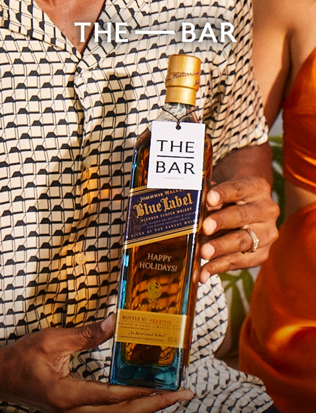 Un hombre sostiene una botella de Johnnie Walker Blue Label grabada con una etiqueta de The Bar visible.