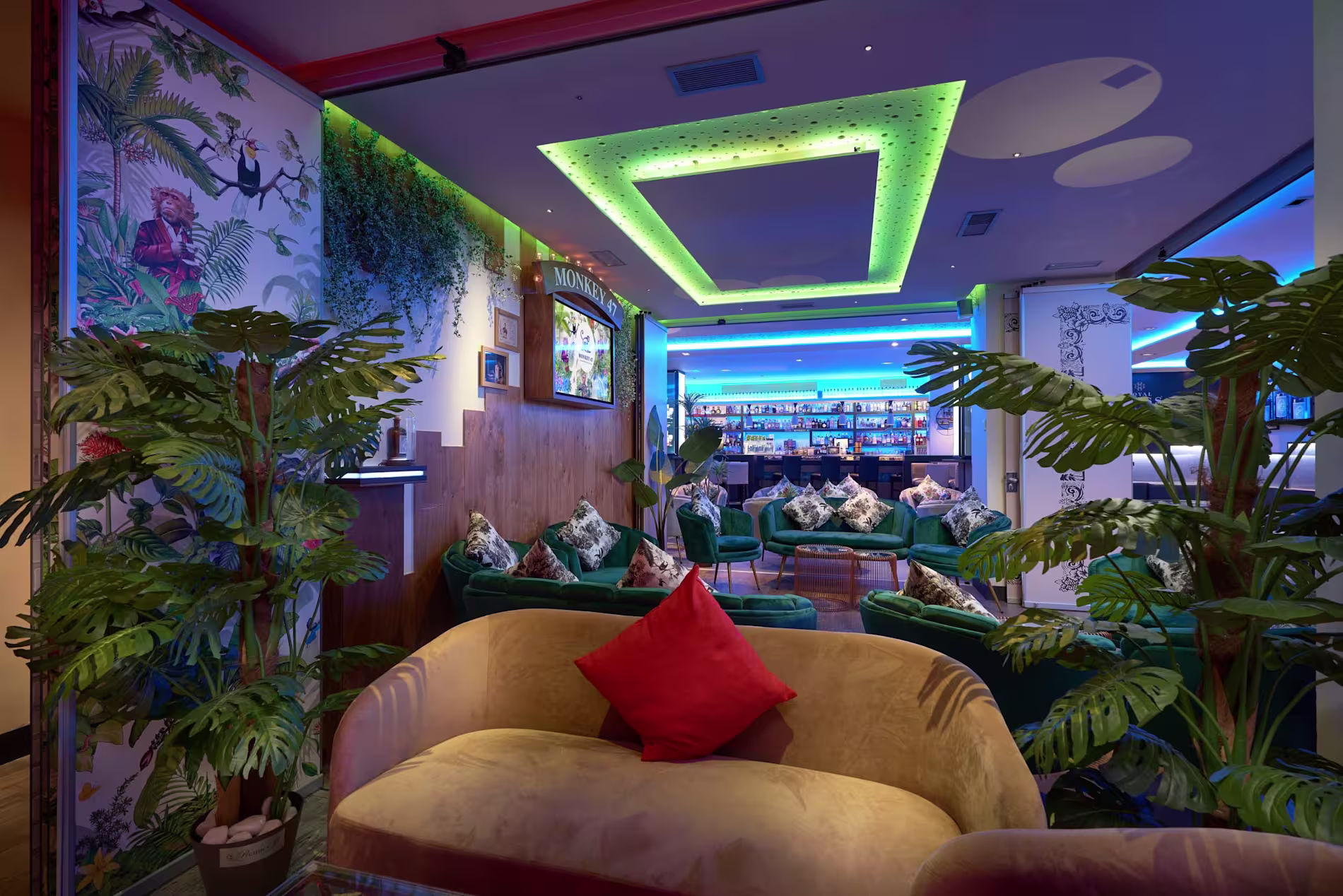Premier Cocktail Gin and Rum Selections con sofás verdes, decoración tropical y luces de neón, ofreciendo un ambiente moderno y relajado.