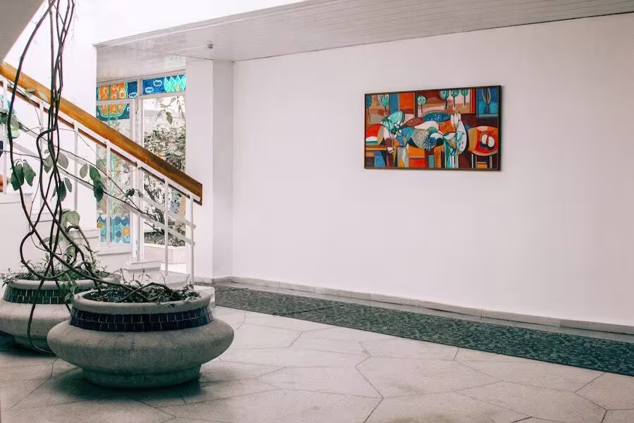 Modern indoor space with two large round planters, a staircase with stained glass panels, and a colorful abstract painting on a white wall.