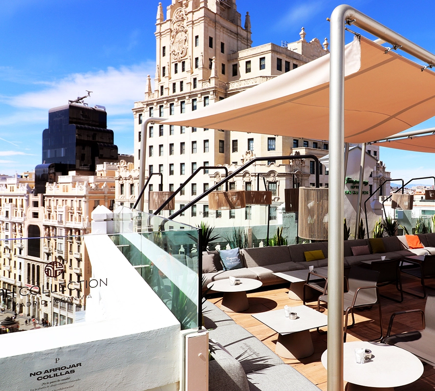 Terraza de Azotea Forus con vistas icónicas de Madrid, decorada con sofás modernos, mesas bajas y un toldo que brinda sombra.