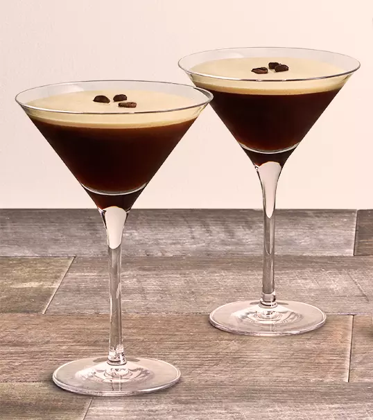 Two espresso martinis in martini glasses, each garnished with three coffee beans, placed on a wooden surface.