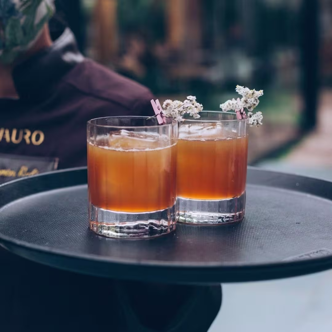 Elegantes cócteles servidos en vasos cortos, adornados con un toque floral, destacando una mezcla balanceada y sofisticada. La presentación es ideal para una experiencia de degustación refinada en un ambiente exclusiv