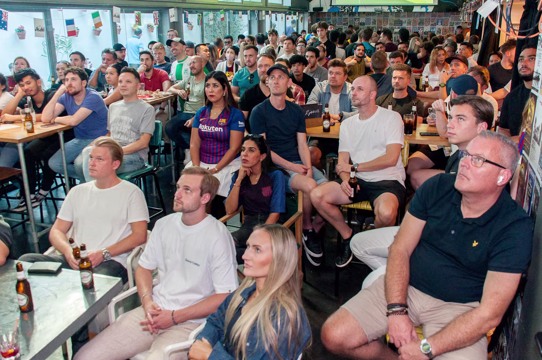La imagen muestra a un grupo de personas en un bar llamado Belushis disfrutando de un partido de fútbol.