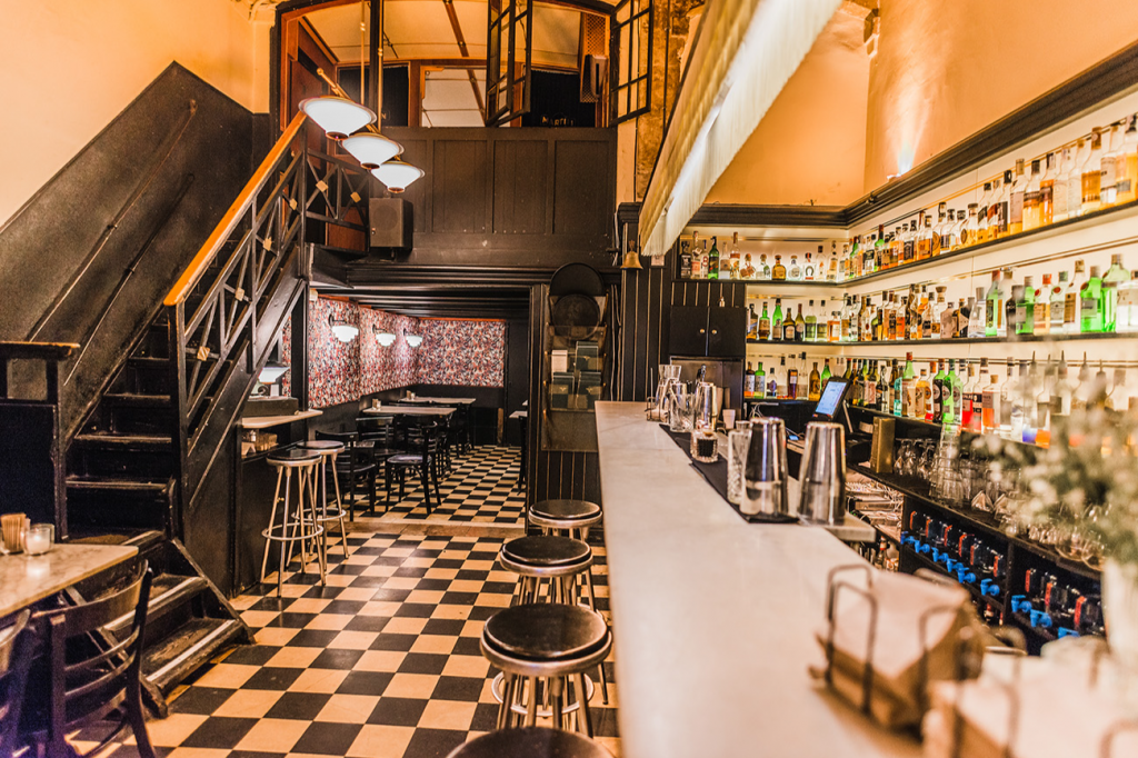 Mudanzas Bar destaca con su diseño vintage, suelos de tablero ajedrezado y una barra iluminada que ofrece un ambiente retro y acogedor.