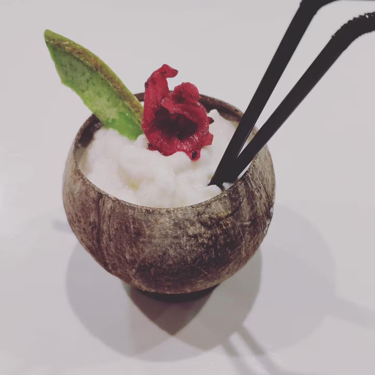 Artadi Beach con un refrescante cóctel tropical servido en un coco, decorado con flor roja y una hoja, ideal para un sorbo exótico.