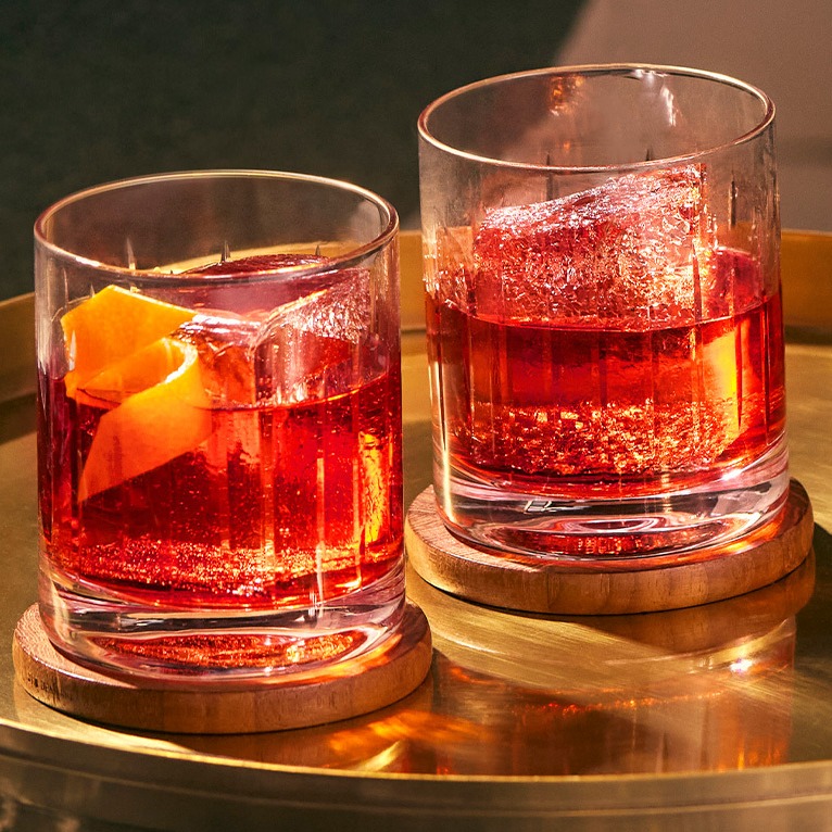Two Negroni cocktails in rocks glasses on a bronze platter.