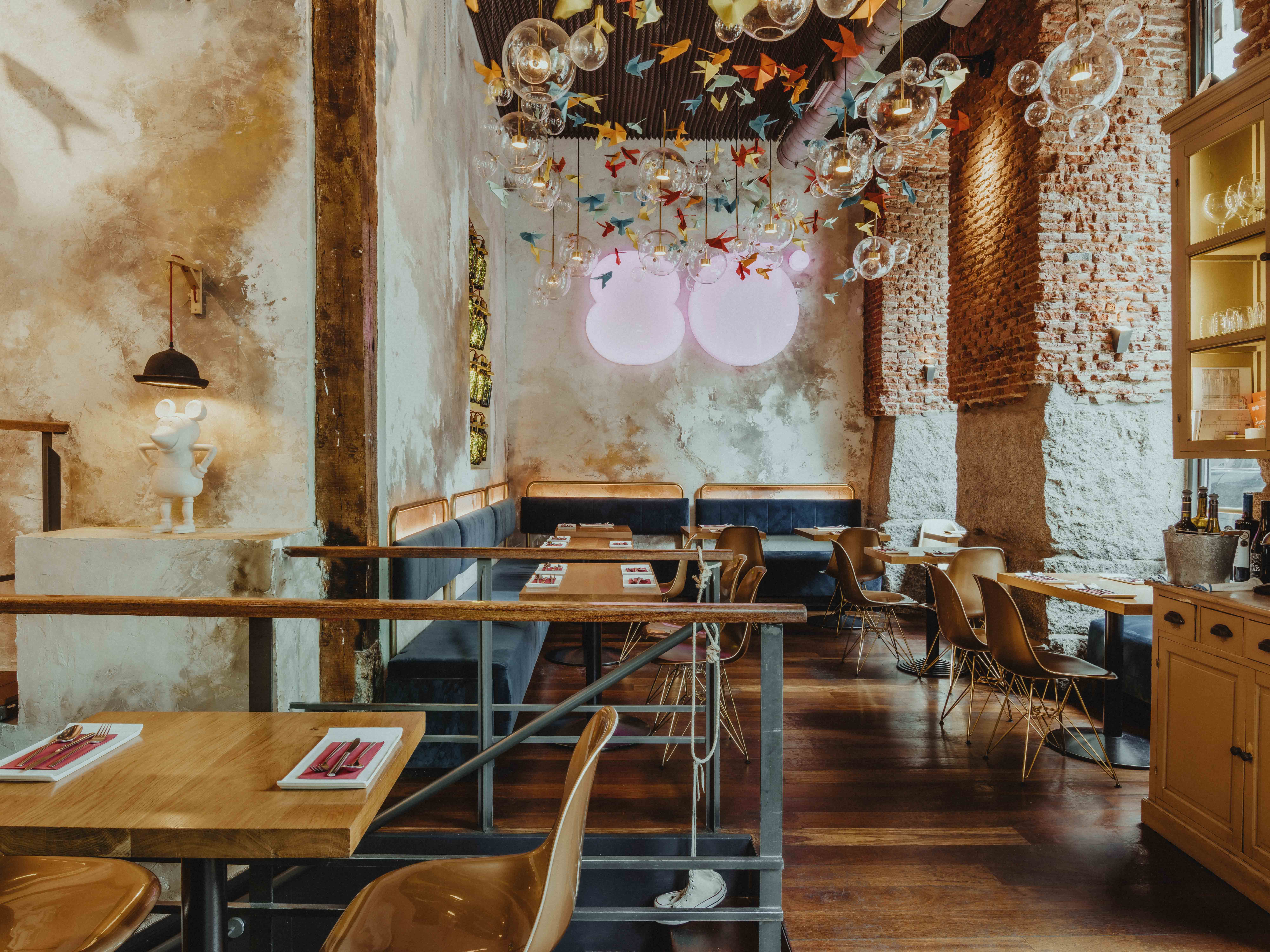 Interior de Ochenta Grados Malasaña con paredes de ladrillo visto, lámparas con burbujas de cristal y grullas de colores colgantes sobre mesas de madera.