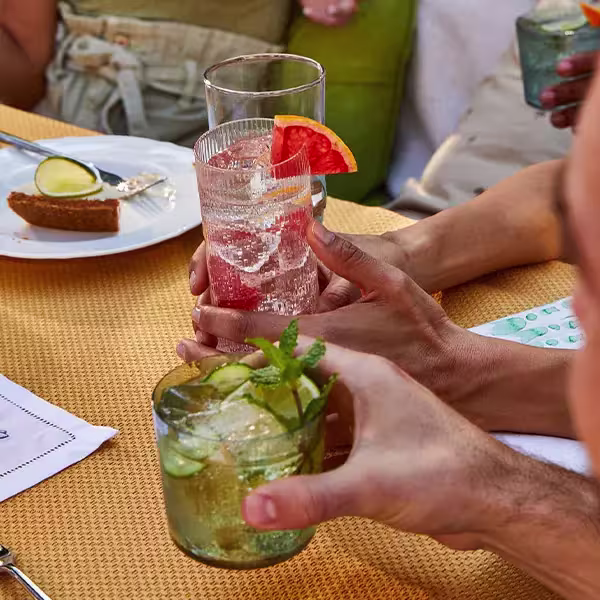 People holding cocktails at an outdoor table set with drinks and a dessert plate.