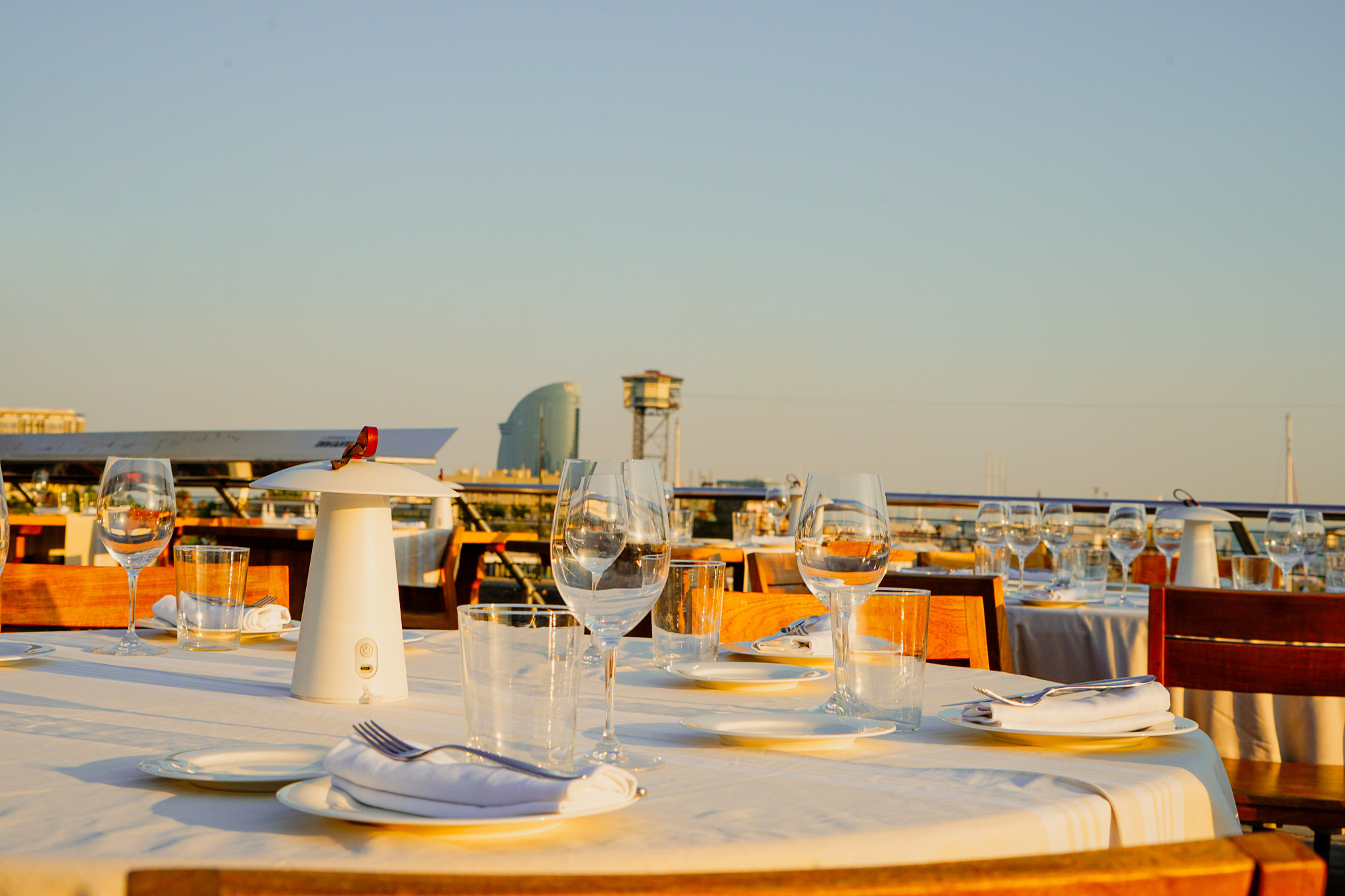 Una mesa al aire libre en el restaurante 1881 per Sagardi , preparada para una comida.
Hay varias copas de vino, cubiertos envueltos en servilletas blancas y un pequeño portavelas.